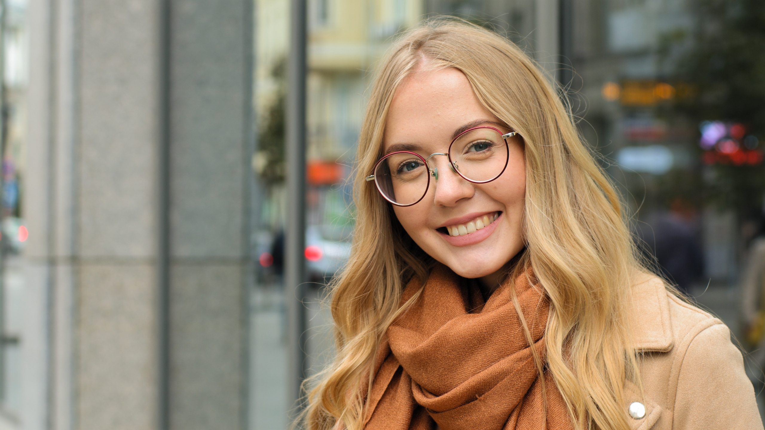 A cheerful young woman wearing trendy round eyeglasses stands outdoors in the city, showcasing modern eyewear style and clear vision – Eyeglasses in Dearborn.