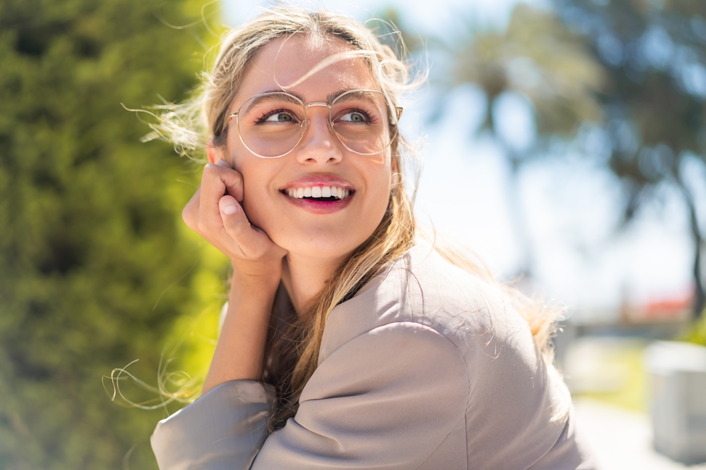 A joyful woman wearing stylish eyeglasses smiles in the sunlight, reflecting comfort, fashion, and clear vision – Eyeglasses in Dearborn.