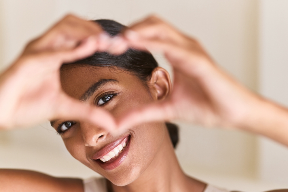 A smiling woman frames a heart shape with her hands in front of her face - Eye Doctor in Dearborn A smiling woman frames a heart shape with her hands in front of her face - Eye Doctor in Dearborn